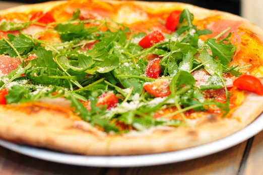 Frisch gebackene Pizza mit Rucola, Tomaten und Käse auf einem Teller angerichtet